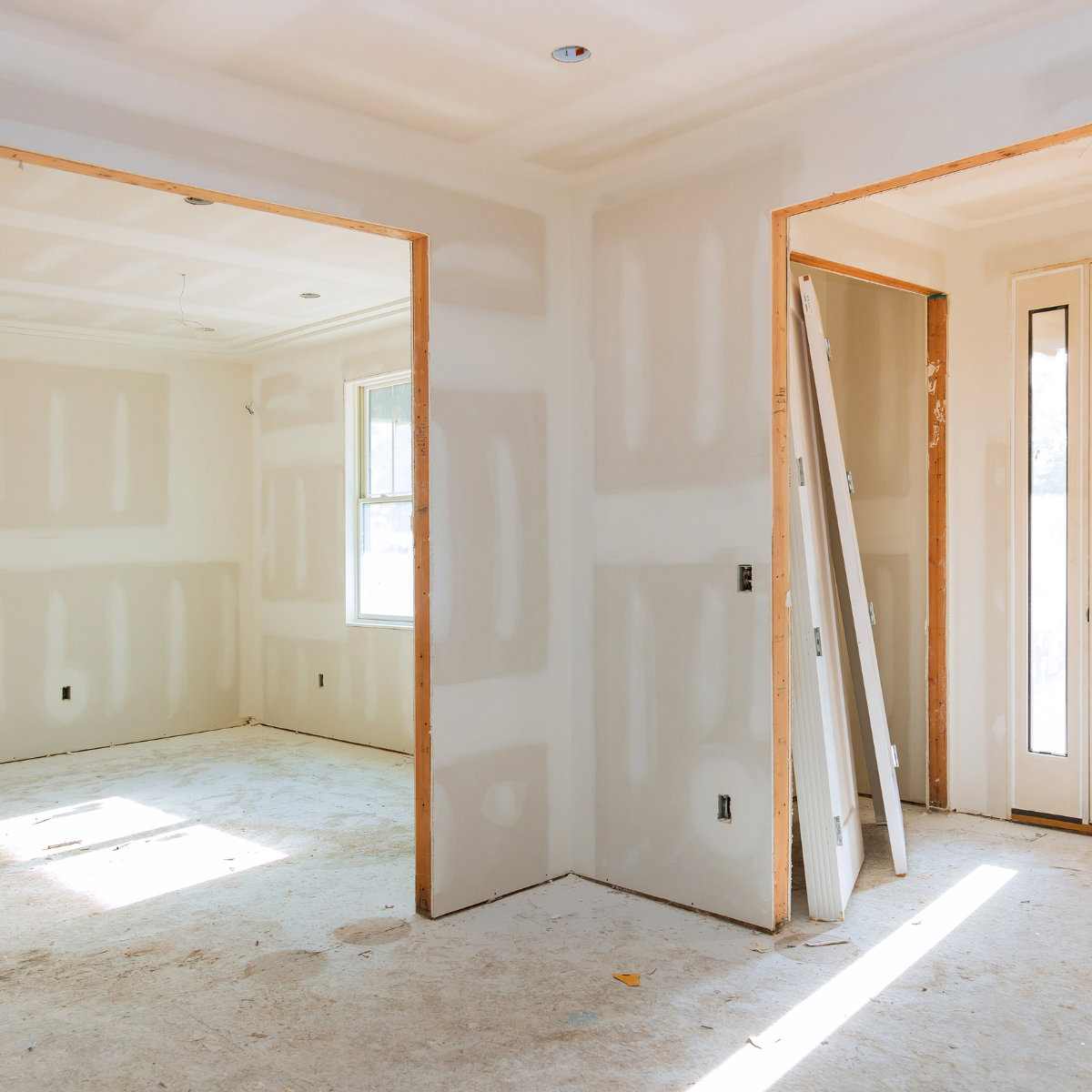 Interior residential construction site showing recently installed drywall, joint compound applied (taped and spackled), and framed door openings awaiting trim and doors.