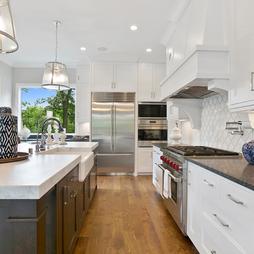 High-end kitchen remodel featuring white shaker cabinets, dark brown island cabinetry, farmhouse sink, professional stainless steel appliances, dark stone countertops, and a white arabesque tile backsplash.