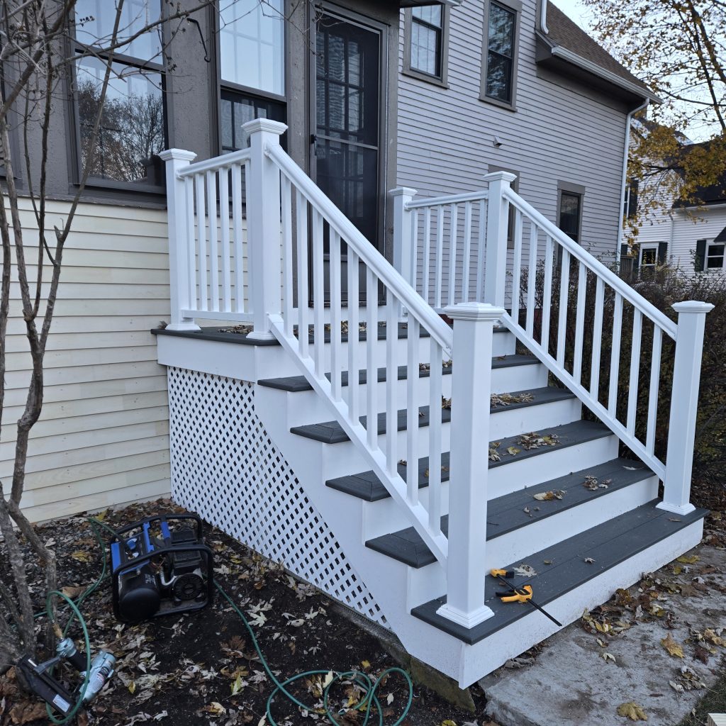 A newly installed side entry featuring grey composite stair treads and white vinyl railings, providing a durable and maintenance-free solution for this NH home.