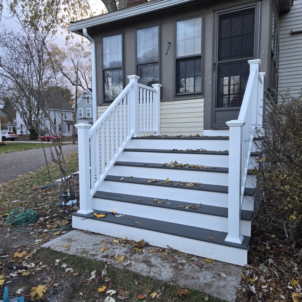 Newly built grey composite deck stairs with white vinyl railings and lattice skirting, featuring tools on the ground during a project in NH.
