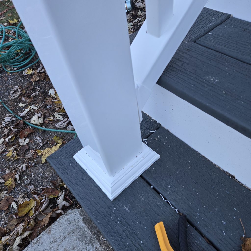 Close-up detail of a white vinyl railing post skirt installed on grey composite stair treads, showcasing clean finish work on a deck project in NH.