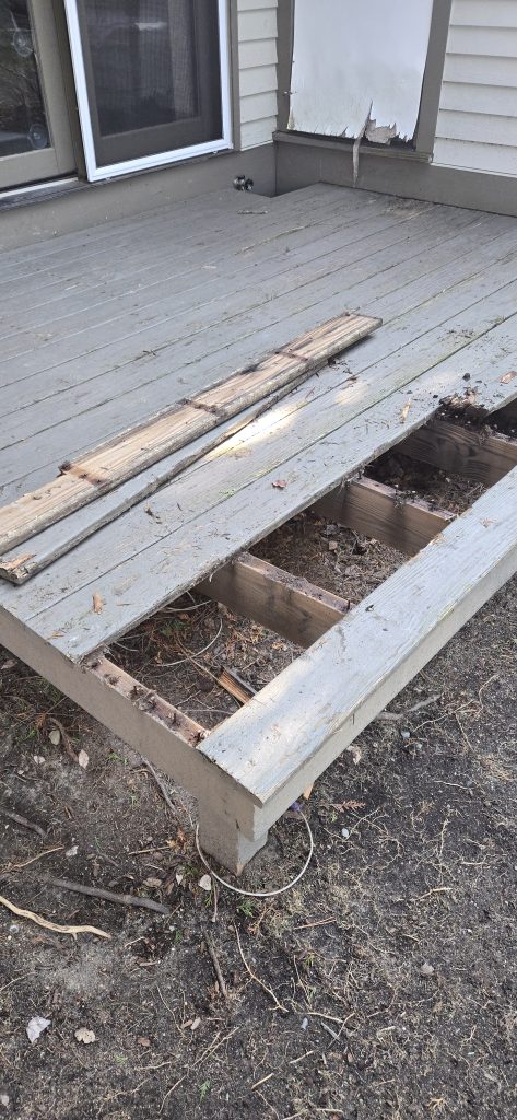 Rotted grey deck boards being removed to expose the underlying wooden joists during a deck resurfacing project in Dover, NH.