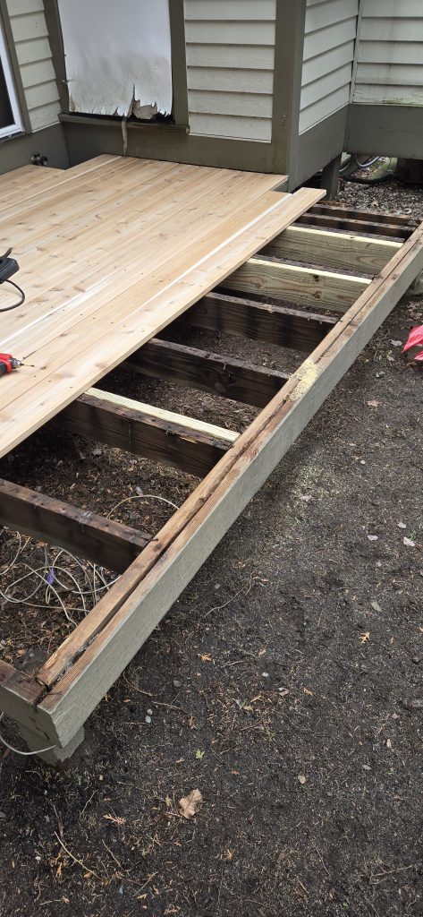 Fresh cedar deck planks being installed over an existing structural frame, with a red power drill resting on the beautiful new wood surface.