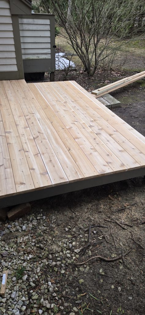 Angled view of a freshly rebuilt cedar deck surface showing clean installation lines, natural wood grain, and fresh decking screws.