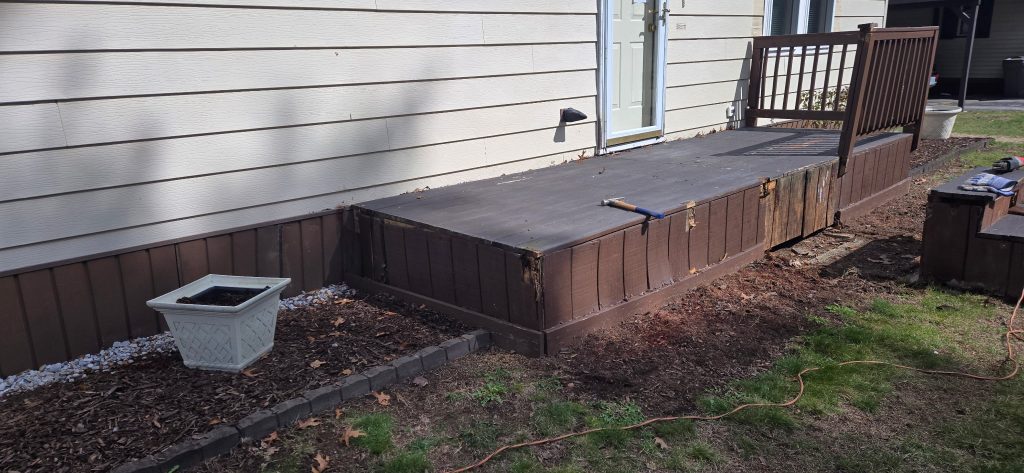 Demolition in progress on a decaying front porch landing, showing the old detached stairs and rotting wood fascia, prior to a safe entry step replacement in Goffstown, New Hampshire.
