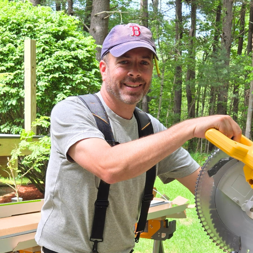 Bob, the owner of Chippy's Handyman, smiling at an outdoor job site while working with a miter saw on a recent New Hampshire build.