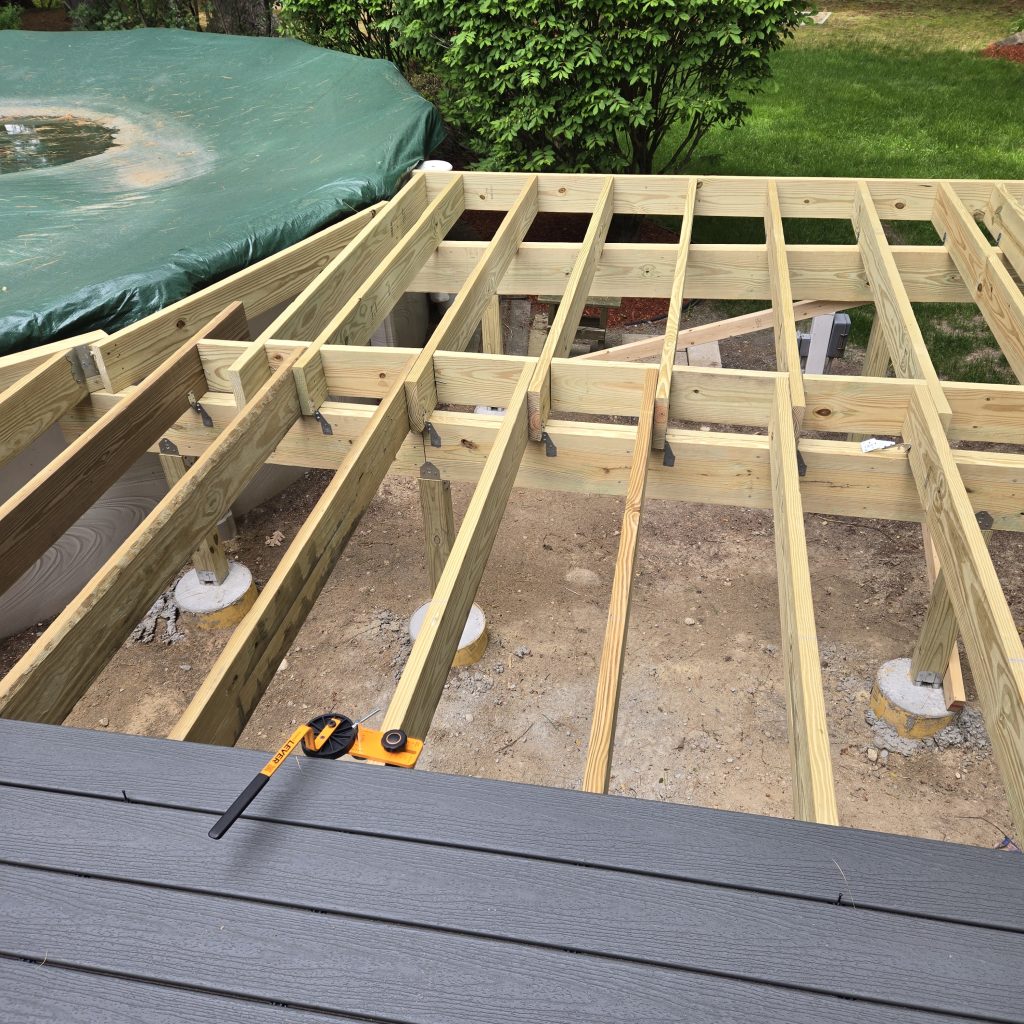 Wooden deck floor joists and frame construction underway next to a backyard pool