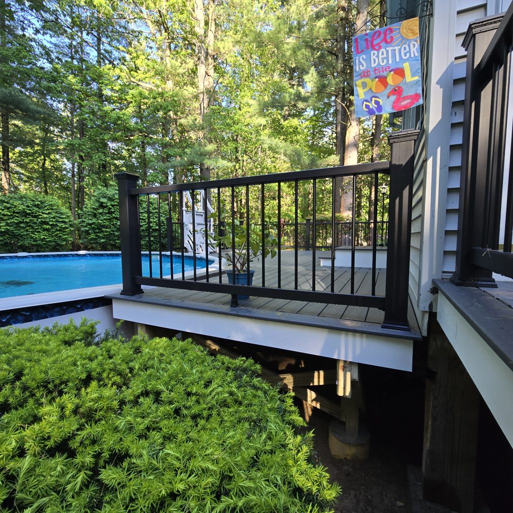 Finished gray composite deck side profile with black metal balusters overlooking a backyard pool