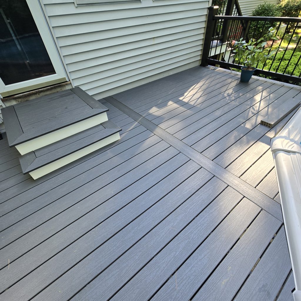A newly built gray composite deck featuring a custom picture-frame border, parting board, and wide entry steps leading to a sliding door, installed by a custom deck builder in Londonderry, New Hampshire.