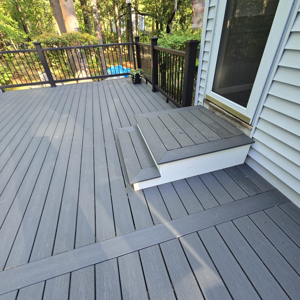 Detail view of a newly built gray composite deck featuring a custom picture-frame border and matching wide entry steps