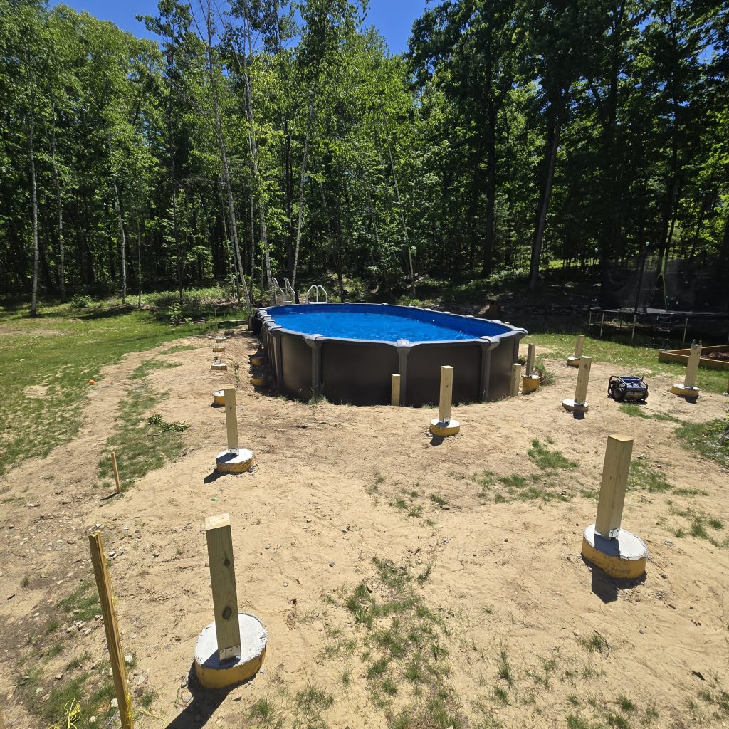 Concrete footings and pressure-treated wood support posts installed around a backyard swimming pool