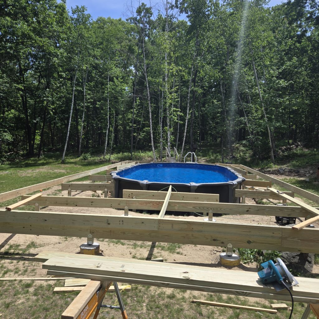 Early construction phase of a custom above-ground pool deck showing the pressure-treated support beams and concrete footings being installed