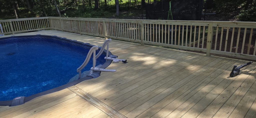 A freshly built pressure-treated wood pool deck being cleaned off, showcasing the expansive custom deck boards and safety railings
