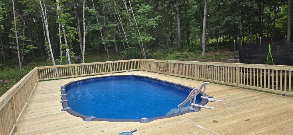 Expansive wooden deck with safety railings built around a backyard above-ground pool in Londonderry, NH