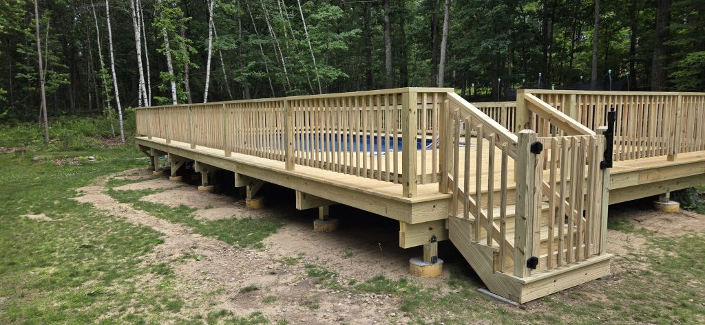 A newly constructed pressure-treated wood pool deck featuring secure railings and a safety gate at the top of the stairs, built by a custom deck builder in Londonderry, New Hampshire.